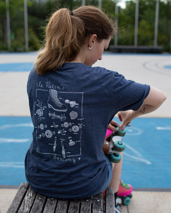 t-shirt the patin's anatomy porté par une jeune femme, vue de dos, assise sur un banc, en train de resserrer les roues de ses patins à roulettes roses